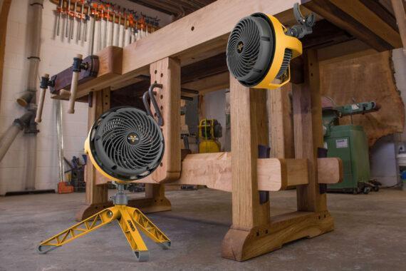 Lifestyle of two EXO5 heavy duty small air circulators in a garage. One is on the floor and the other is clamped to the side of a work table.