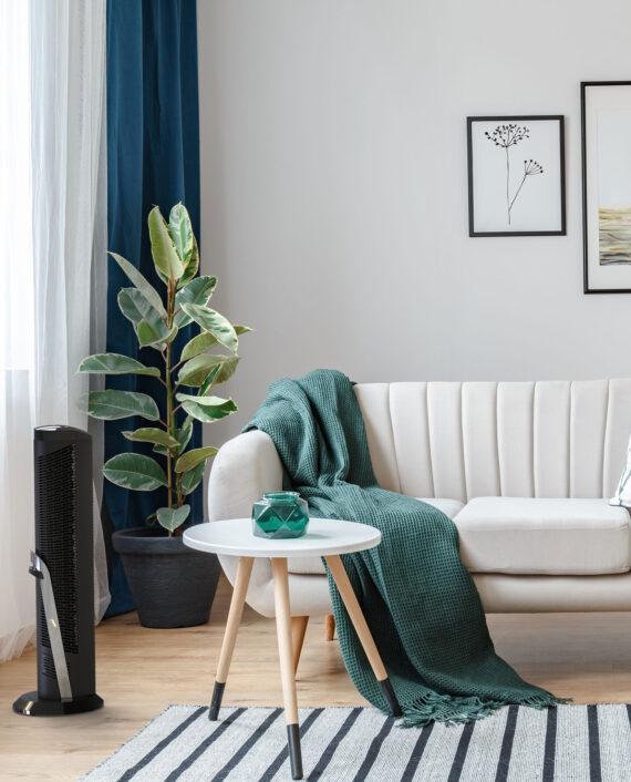 Lifestyle of a Black OSCR32 Oscillating tower circulator in a living room by a small side table and cream colored couch.