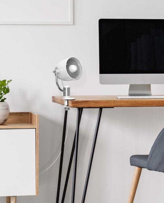 lifestyle image of a White Pivot Clip Personal Air Circulator clipped to the side of a wood desk.