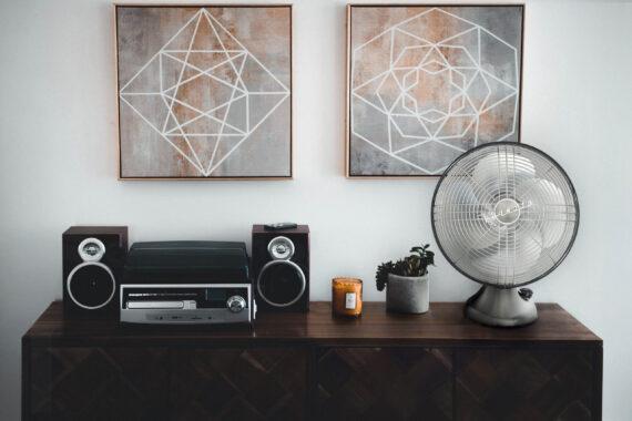 Lifestyle of a Silver Swan Vintage Oscillating Fan on a wood side table with a plant, a candle, and stereo.