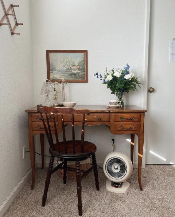 Image of a VHEAT Vintage White under a traditional style wooden desk that has a vase of flowers and a small catch-all bowl on top of it